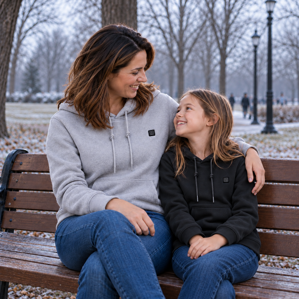 Woman and girl wearing grey and black Caldris hoodies, seated together on a park bench.