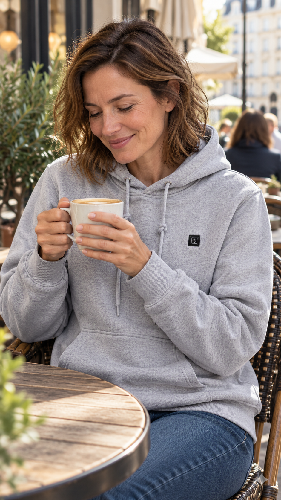 Adult woman wearing a grey Caldris hoodie at a café, illustrative scene.